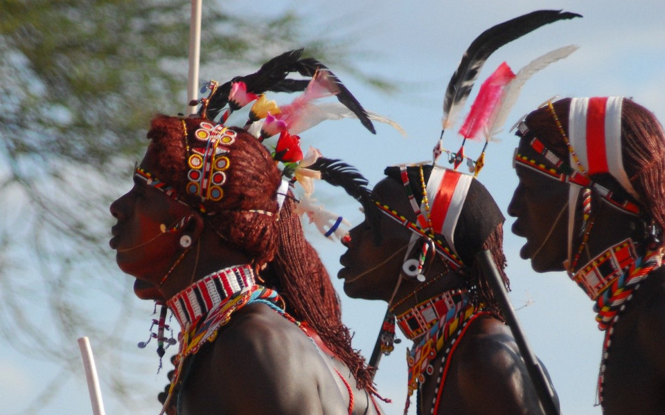 M&auml;nner in traditioneller Kleidung mit buntem Schmuck und Federn, die in einer Zeremonie in Kenia teilnehmen.